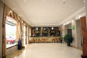 A spacious lobby with a marble floor, a reception desk, and a large window with curtains.
