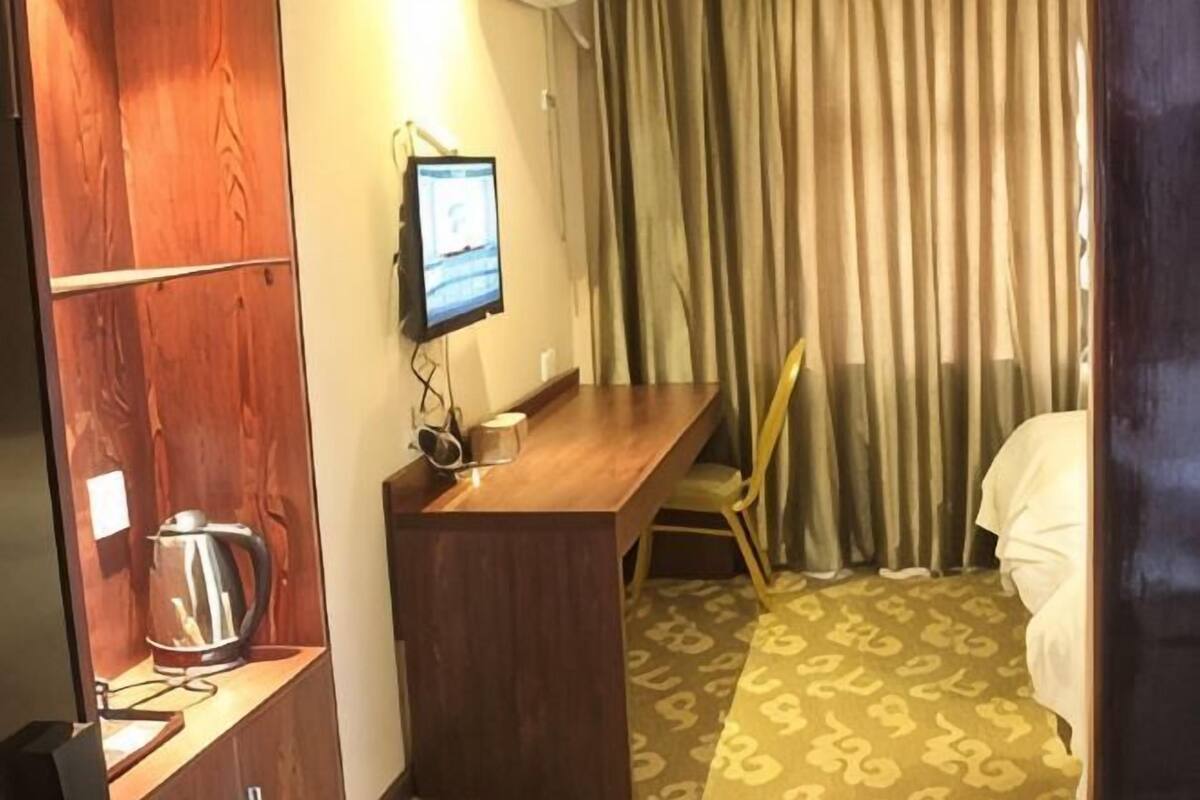 Une chambre d’hôtel avec un bureau en bois, une télévision, une machine à café, une moquette à motifs et un lit avec des rideaux.