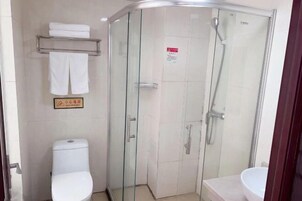 Un baño en esquina con ducha de vidrio, inodoro y lavamanos.