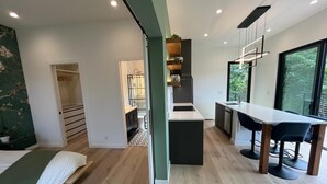 Ein moderner, offener Wohnbereich mit Schlafzimmer und Küche, mit Holzboden, einem Bett, einem Esstisch mit Stühlen und Blick durch große Fenster.