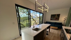 Eine moderne Küche mit einer großen Kochinsel, einem Essbereich inklusive Sofa und Blick auf Bäume durch große Fenster.