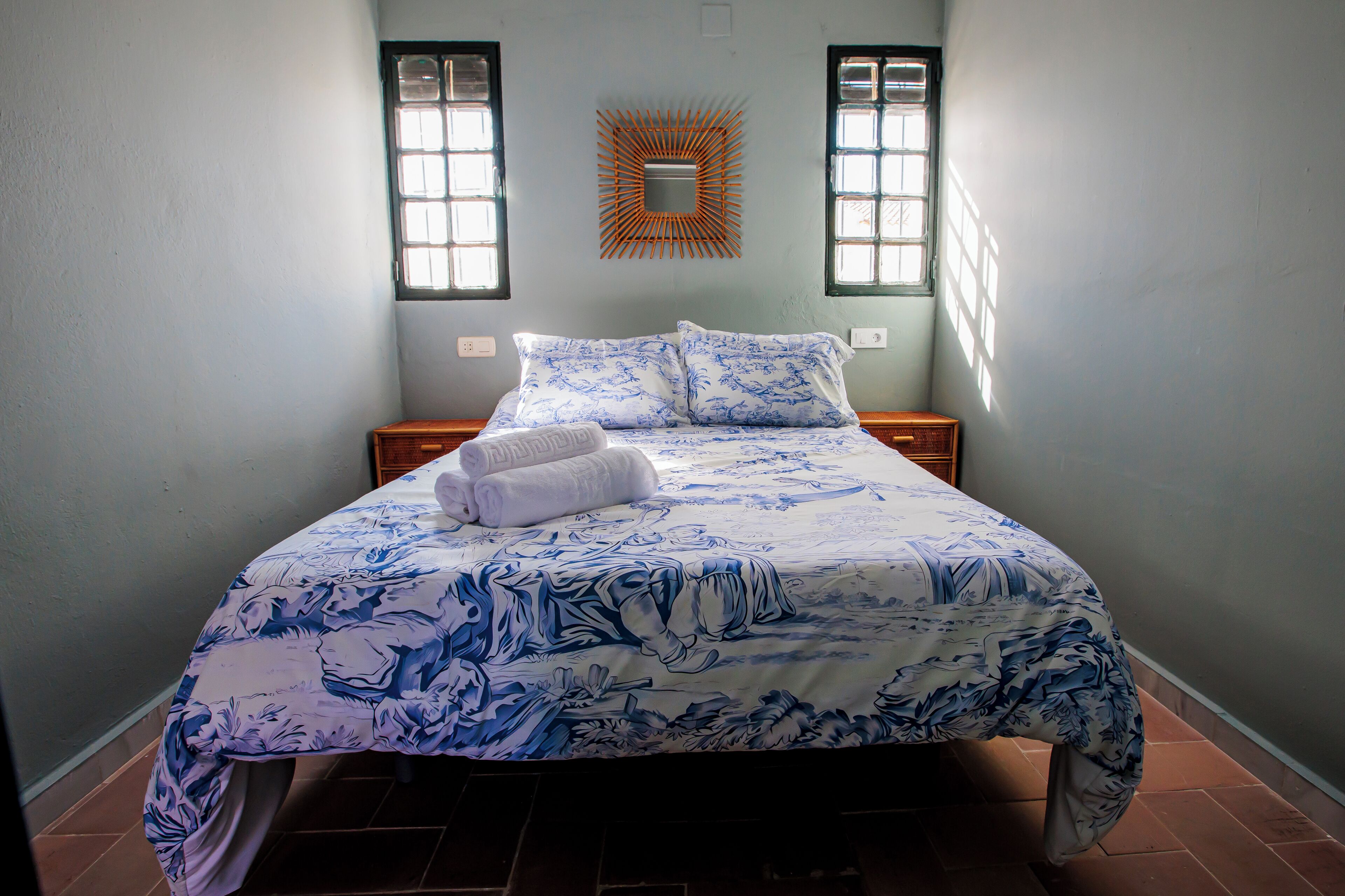 A bed with a floral bedspread, two pillows, and a folded towel on the side.