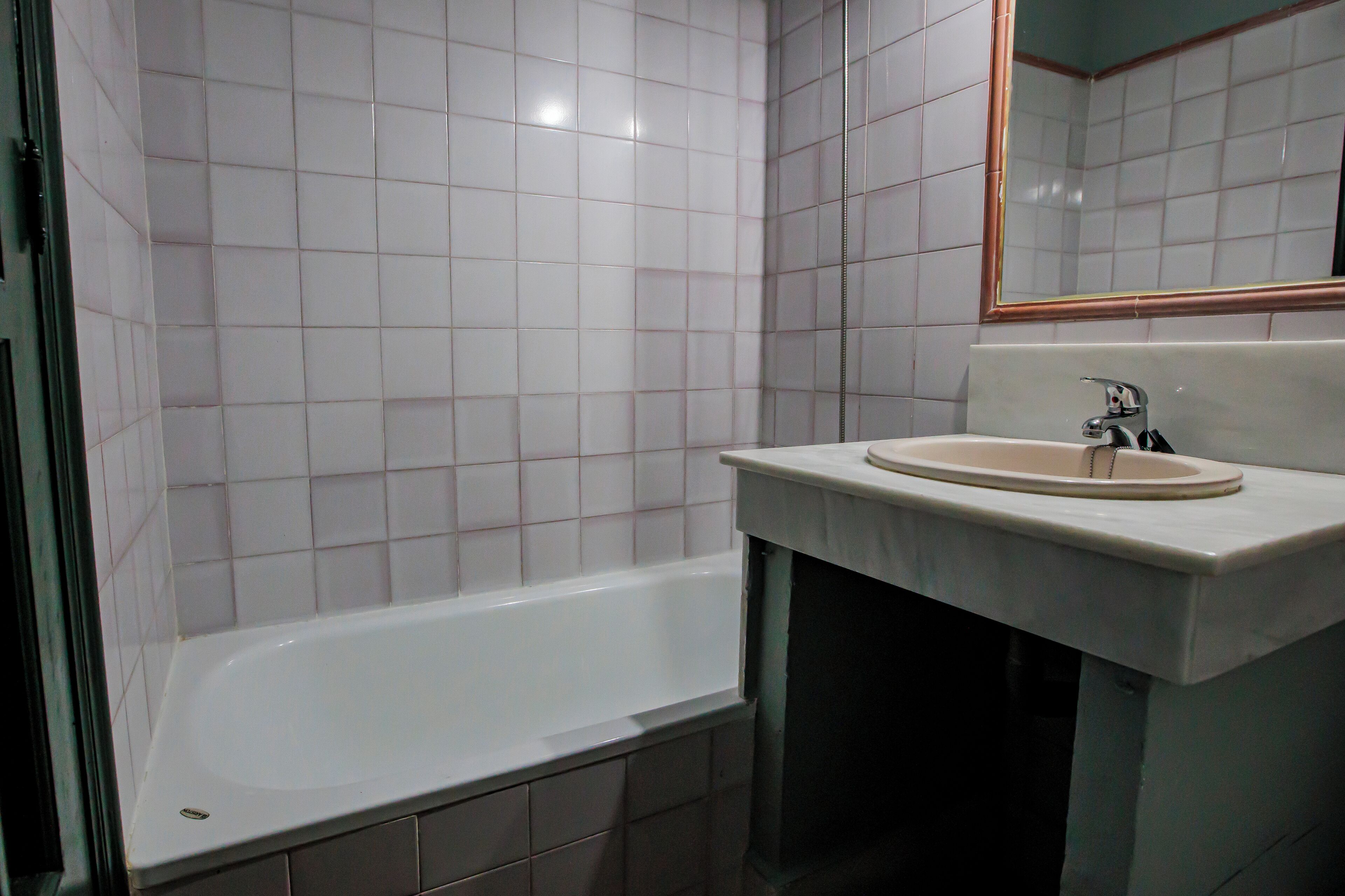 Un baño con una bañera blanca, un lavabo con un espejo encima y paredes con azulejos.