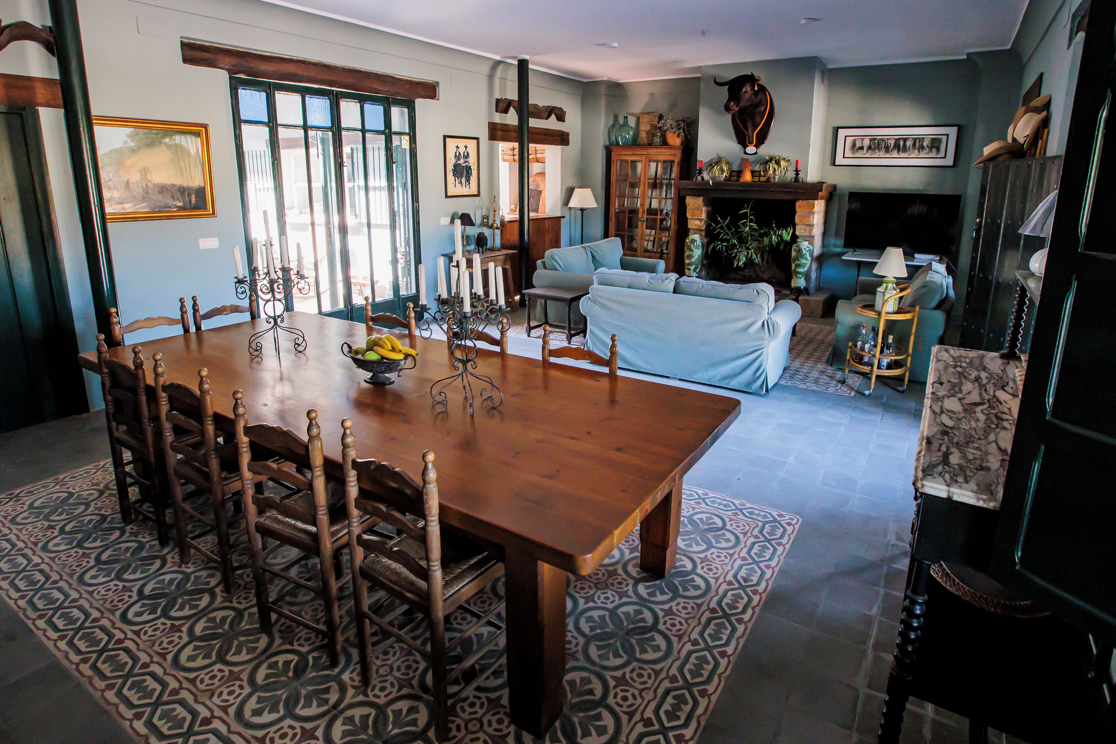 Un coin repas avec une table et des chaises en bois, un tapis à motifs, et un salon avec un canapé et une cheminée.