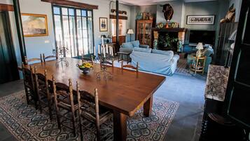 Un coin repas avec une table et des chaises en bois, un tapis à motifs, et un salon avec un canapé et une cheminée.