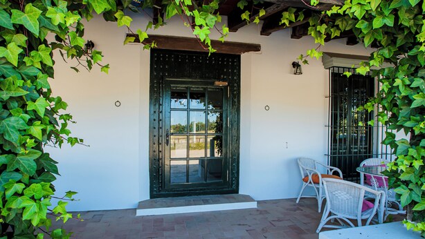 A patio with a black door, white wicker furniture, and green vines. - HN Romero 18 (Almonte)