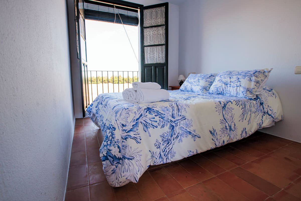 Un dormitorio con cama, mesita de noche, ventana con vistas y puerta.