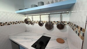 Une cuisine dotée d’un plan de travail en marbre blanc, d’une plaque de cuisson à induction noire et de casseroles suspendues à un étendoir.