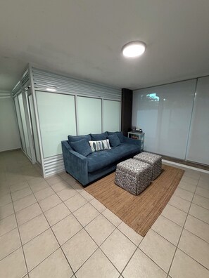 A living room with a sofa, ottoman, and a small table with items on it.