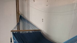 Un'amaca con coperta azzurra all'uncinetto, fissata a un palo di legno, su un pavimento in cemento.