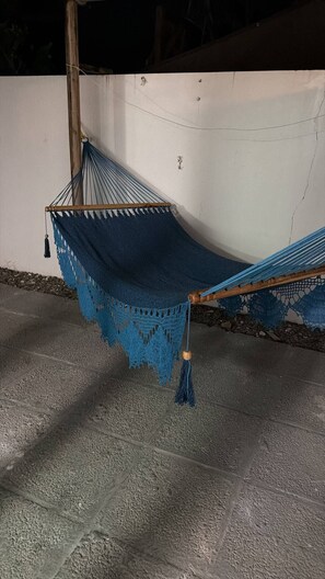 A hammock with a blue crocheted cover, attached to a wooden post, on a concrete floor. - One minute walk to the beach! (Luquillo)