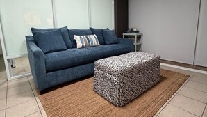 Un soggiorno moderno con un divano blu, un poggiapiedi fantasia e un tappeto intrecciato.