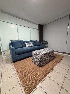 A modern living room with a blue sofa, patterned ottoman, and a woven rug. - One minute walk to the beach! (Luquillo)