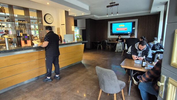 A modern bar area with a counter, seating, and a TV screen displaying a program. - Duisburger Hostel (Duisburg)