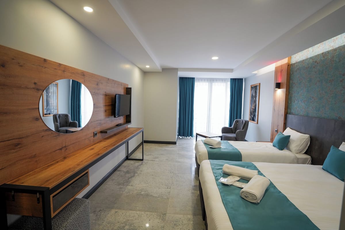 A hotel room with two beds, a wooden console table, a TV, and a large mirror.