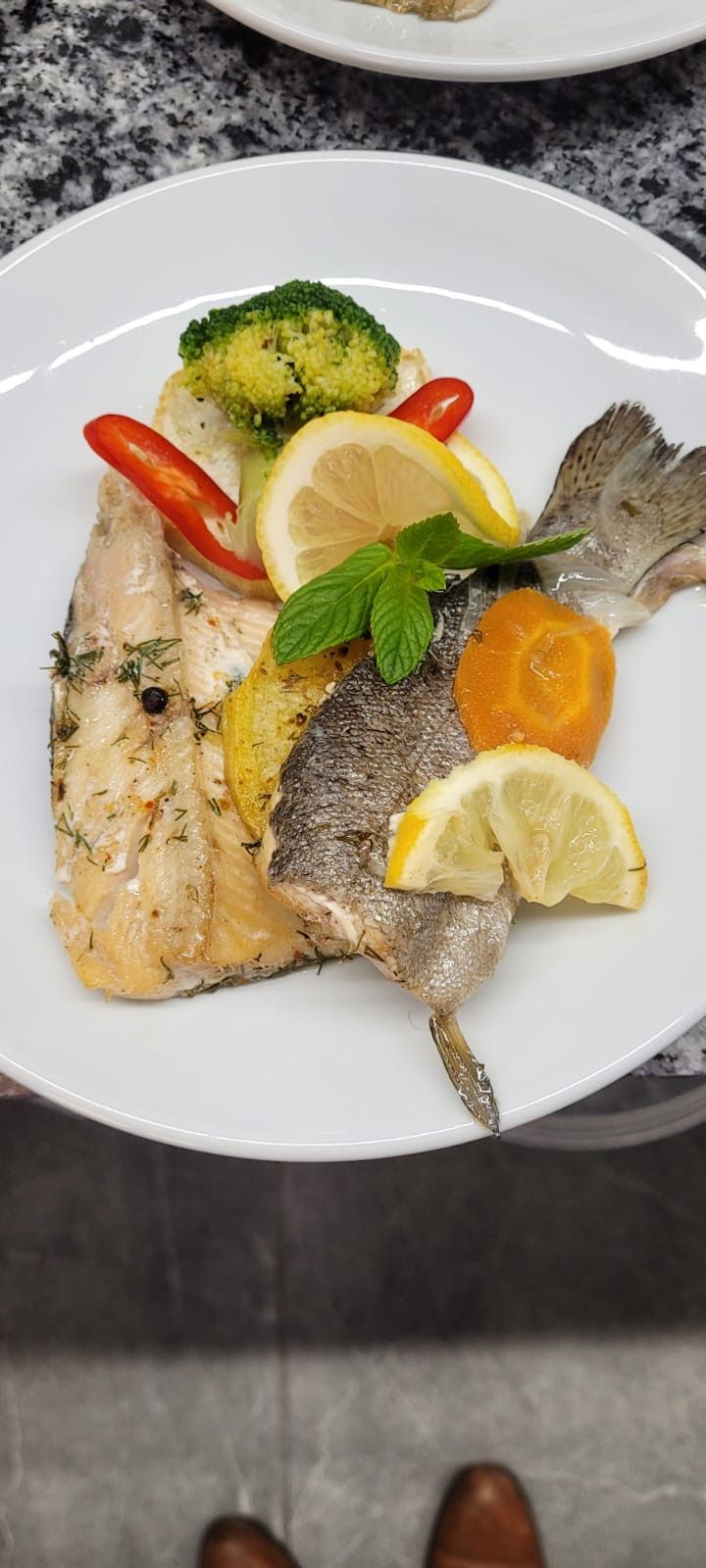 Un plato con pescado, limón y verduras.
