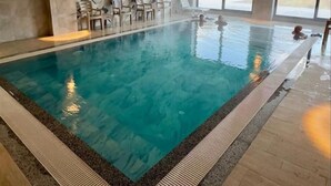 An indoor swimming pool with clear blue water, surrounded by a tiled floor and a patterned wall. - Çelik Thermal & Spa (Denizli)