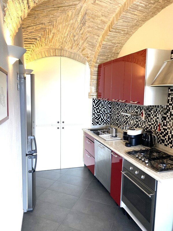A kitchen with a checkered backsplash, red cabinets, a stainless steel refrigerator, and a gas stove.