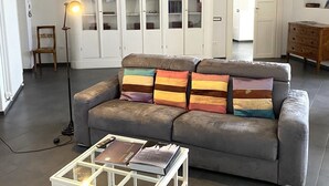 Sala de estar con un sofá gris, una mesa de centro blanca con libros, una lámpara de pie y un techo decorativo.