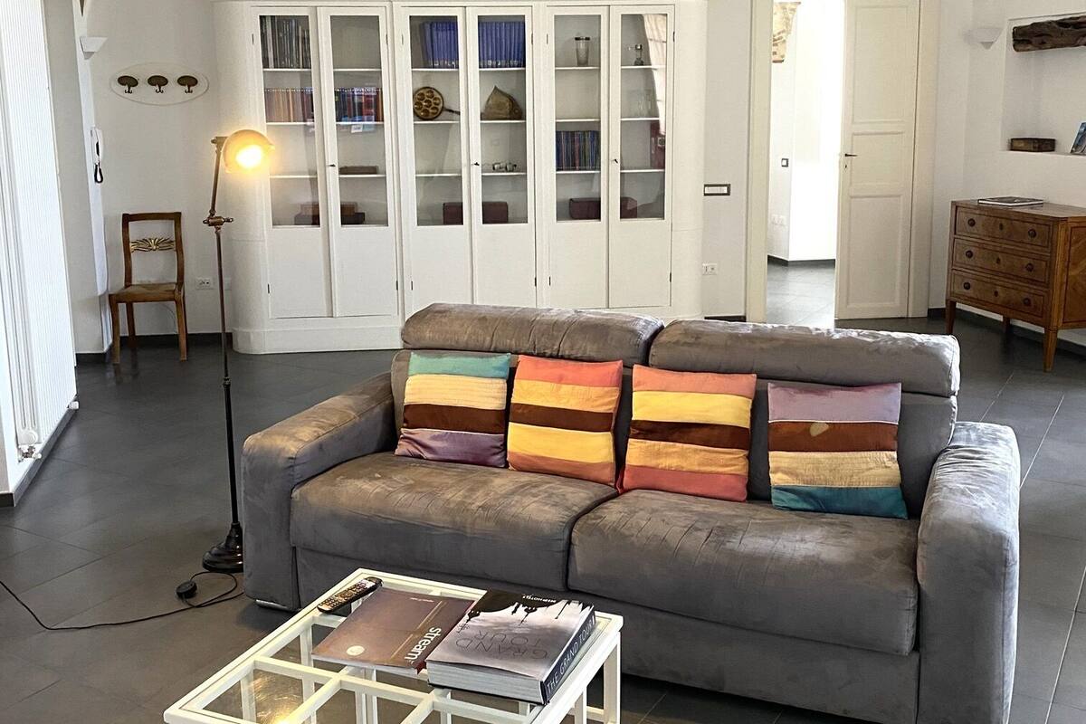 A living room with a grey sofa, a white coffee table with books, a floor lamp, and a decorative ceiling.