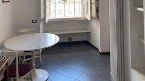 Una habitación con techo de ladrillo, una mesa blanca con una silla, una ventana con barrotes y un radiador.