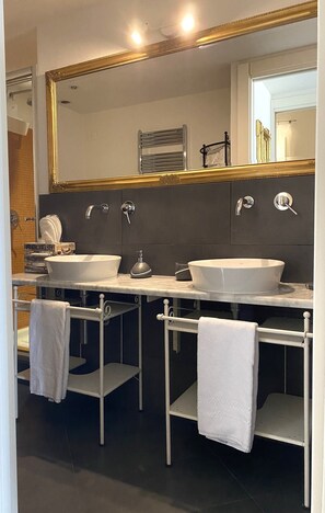 A modern bathroom with two sinks, a large mirror, and a towel rack. - CMH Castello Suites (Cagliari)