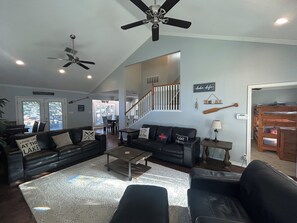 Ein geräumiges Wohnzimmer mit hoher Decke, Deckenventilator und einer Treppe, die zu einer anderen Ebene führt.