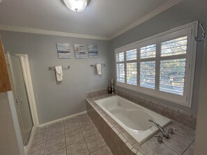 Ein Badezimmer mit einer Badewanne, einem Fenster mit Jalousien und einer Tür.