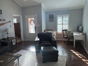 A living room with a black leather sofa, a small table, a desk with a computer, and a window with blinds. - Huge property with Lake Access! 8 separate sleeping spaces, 4 baths! (Kingsland)