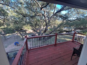 A wooden deck with a red railing, overlooking a fenced yard with trees and a small doghouse. - Huge property with Lake Access! 8 separate sleeping spaces, 4 baths! (Kingsland)