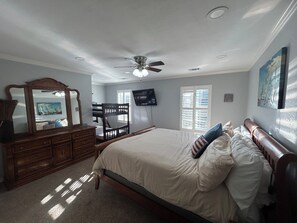 Ein Schlafzimmer mit Bett, Kommode, Spiegel, Deckenventilator, Fernseher, Fenstern und Kunstwerken.