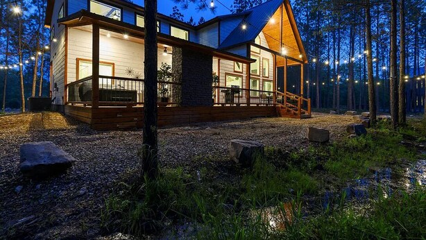 A modern cabin with a deck, surrounded by trees and a gravel path. - HopSquatch: Air Hockey, Hot Tub, Games, Fire Pit, Pet-Friendly, Family-Oriented (Broken Bow)