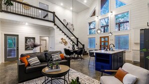 A spacious living area with a high ceiling, a staircase, and large windows. - HopSquatch: Air Hockey, Hot Tub, Games, Fire Pit, Pet-Friendly, Family-Oriented (Broken Bow)