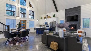 A spacious living area with a fireplace, a dining area with a large table and chairs, and a kitchen with modern appliances. - HopSquatch: Air Hockey, Hot Tub, Games, Fire Pit, Pet-Friendly, Family-Oriented (Broken Bow)