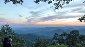 A hiker on a mountain trail with a view of distant mountains and a sunset. - Luxurious Modern Cabin - Timber For Two (Blue Ridge)
