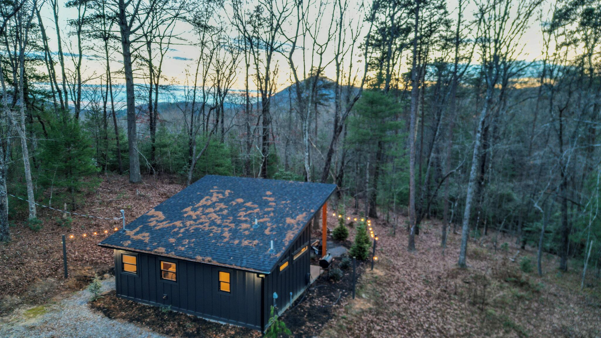 A small cabin with a dark exterior, surrounded by a forested area.