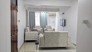 A living room with a sofa, two armchairs, a TV, and a ceiling fan.