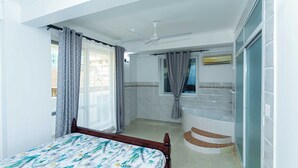 A bedroom with a bed, a ceiling fan, a window with curtains, a bathroom with a bathtub, and a toilet.