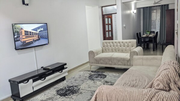 A living room with a flat-screen TV mounted on the wall, a sofa, a coffee table, and a patterned rug.