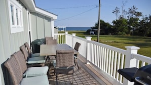 Eine überdachte Terrasse mit Gartenmöbeln, einem Grill und Blick auf den Ozean.