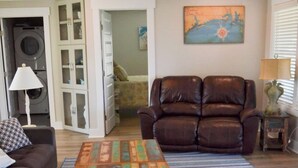 Ein Wohnzimmer mit einer Couch, einem Relaxsessel, einem Couchtisch, einem Deckenventilator und einem Gemälde an der Wand.