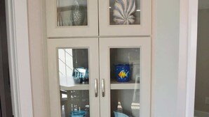 Ein weißer Eckschrank mit Glastüren, der verschiedene Küchenutensilien und Dekorationsgegenstände beherbergt.