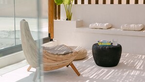 A modern room with a glass partition, a wicker chair, a black ottoman, and a plant. - Villa Aldea - Luxury Boho Style (Rethymno)