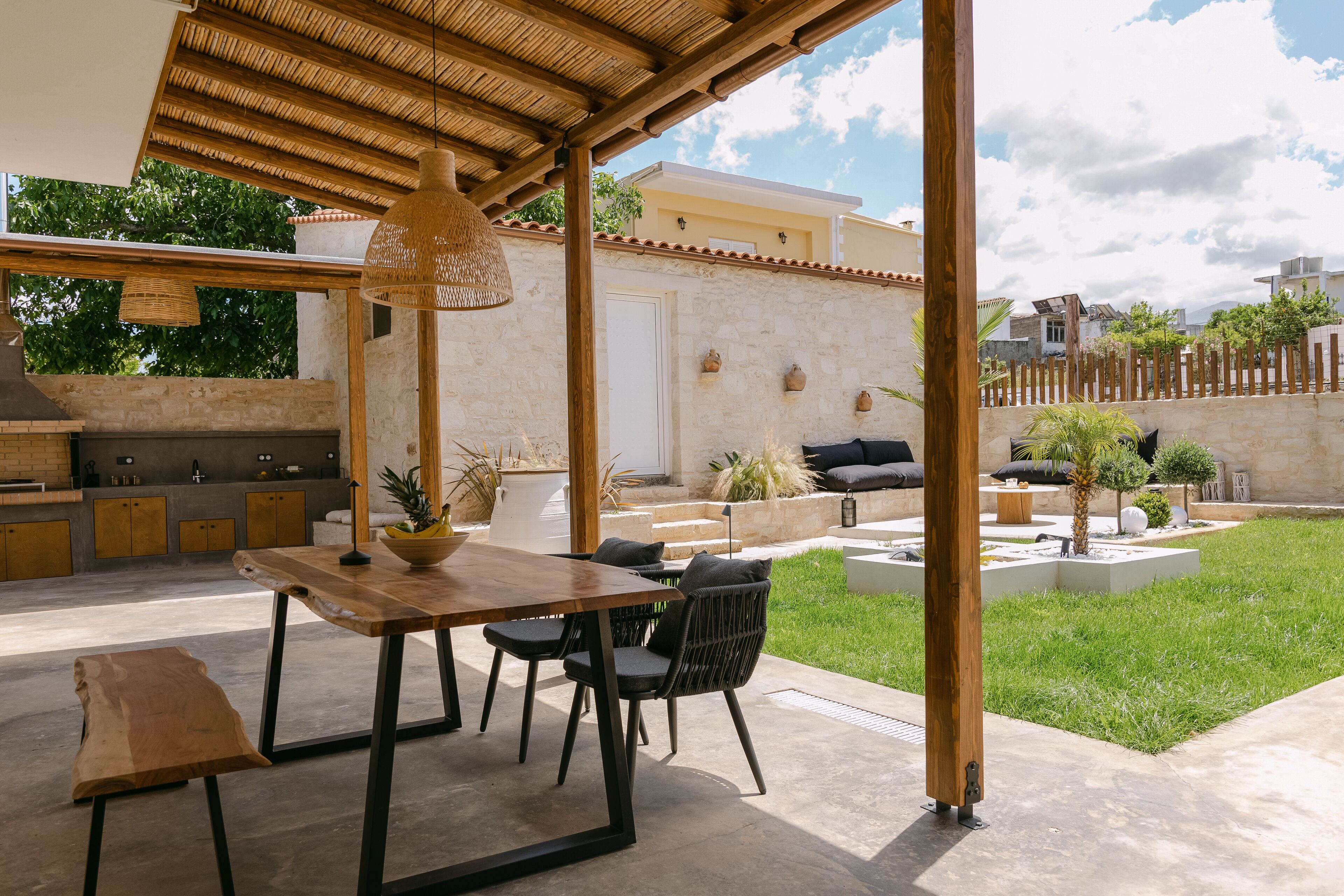 Eine Terrasse im Freien mit Holztisch und -stühlen, einer hängenden Leuchte und einer Steinwand im Hintergrund.