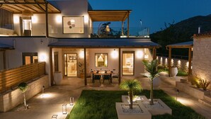 A modern two-story house with a covered patio, a dining area, and a well-lit garden. - Villa Aldea - Luxury Boho Style (Rethymno)