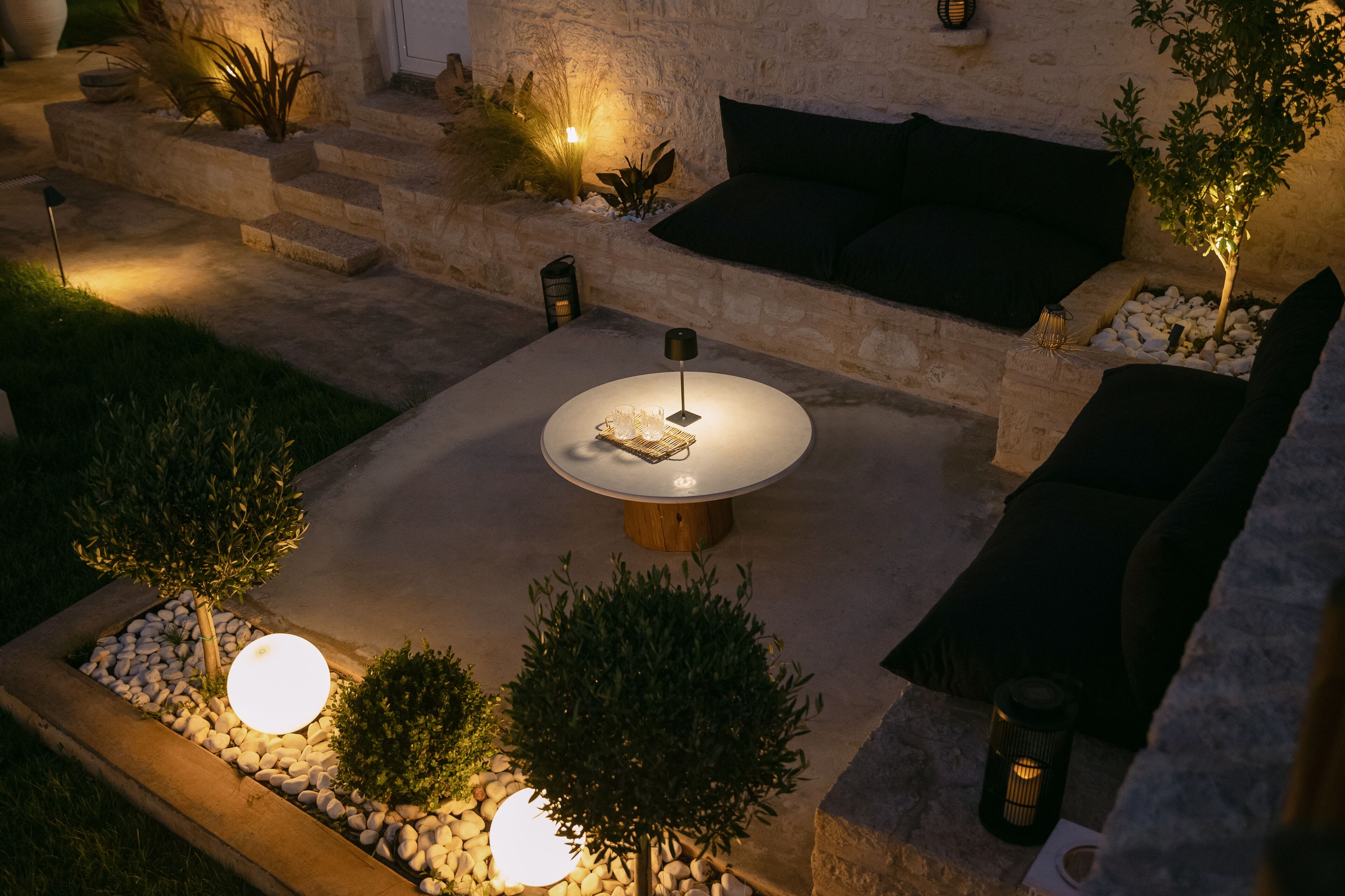 Eine Terrassenanlage im Freien mit einem runden Tisch, Sitzgelegenheiten und dekorativer Beleuchtung.