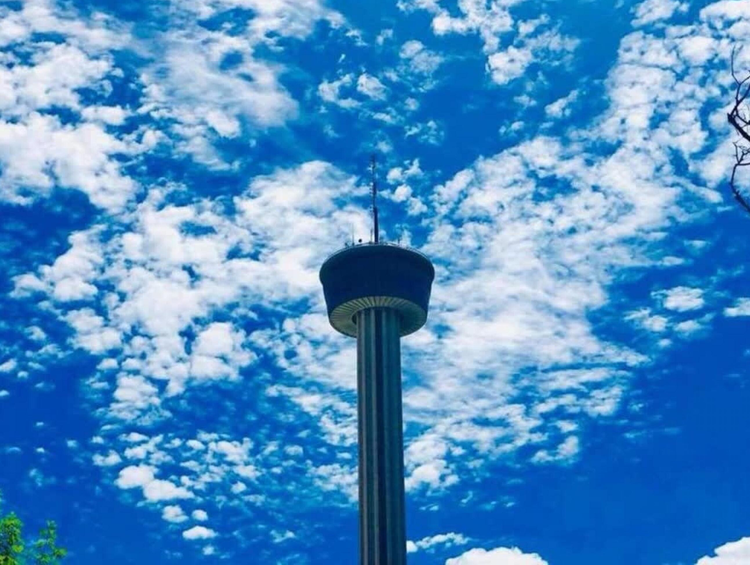 Una torre con una plataforma de observación circular, rodeada por un cielo azul despejado con nubes dispersas.