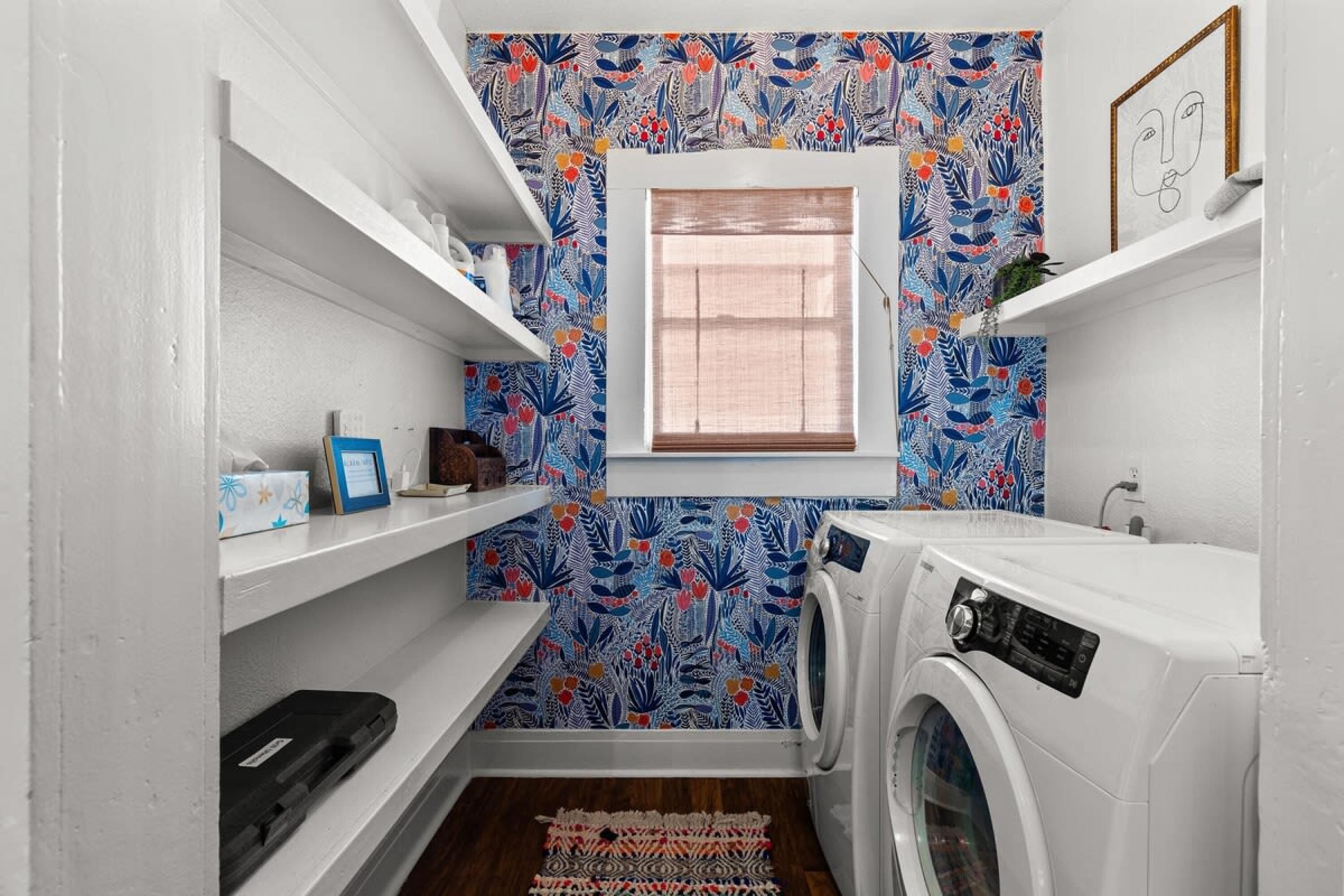 A compact laundry room with a washing machine, shelves with toiletries, and a patterned wall.