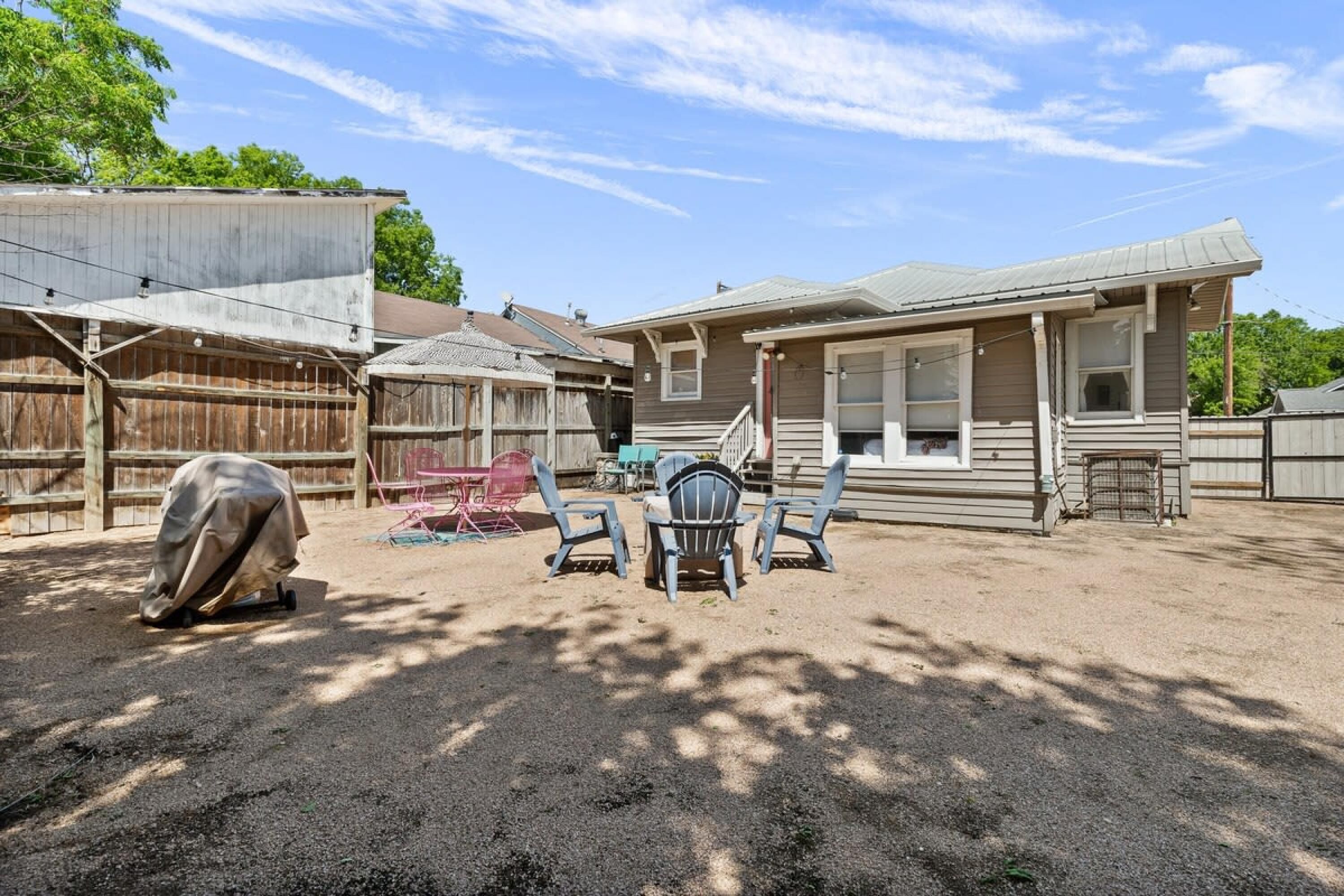 En bostadsträdgård med en täckt uteplats, ett trästaket och ett hus med garage.
