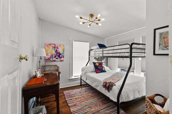 A bedroom with a bunk bed, a desk with a lamp, a colorful rug, and a ceiling light fixture. - Gorgeous Artistic Fully Fenced Home Near Downtown (San Antonio)
